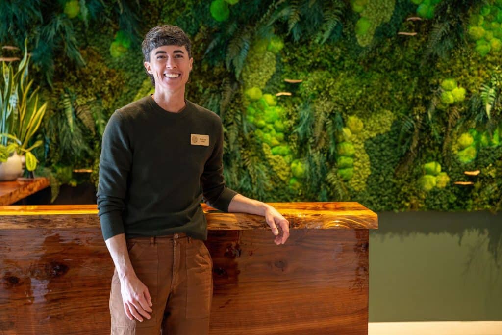 woman standing in front of desk with lush wall behind in the lobby of a funeral home