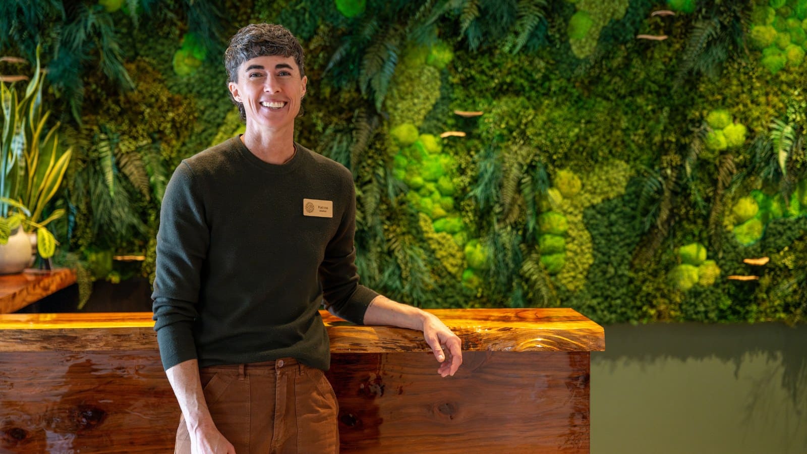 person standing in front of a desk with a lush green wall of moss behind